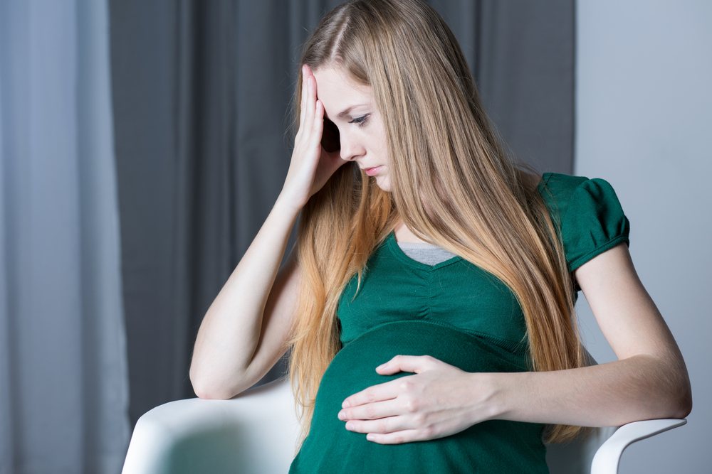 pregnant woman touching her belly and head, sitting on chair