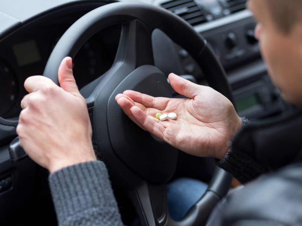 man taking pills while behind the wheel of his car