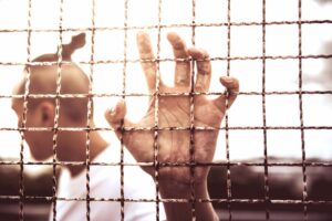 A man with his hand gripping a fence, prison