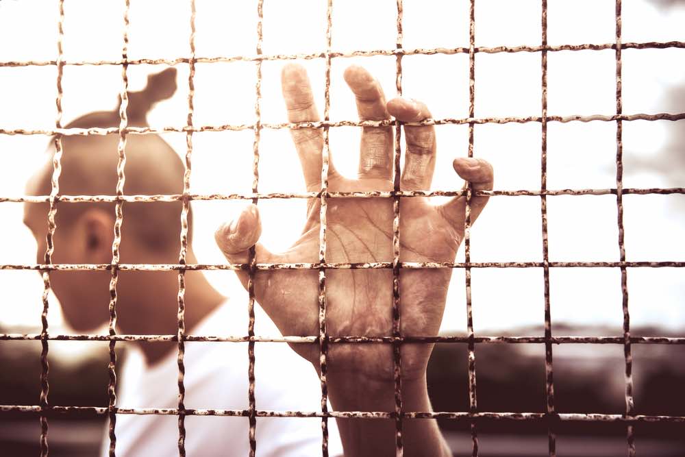 A man with his hand gripping a fence, prison