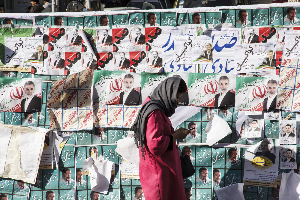 woman walking by campaign posters of Iran parliamentary members