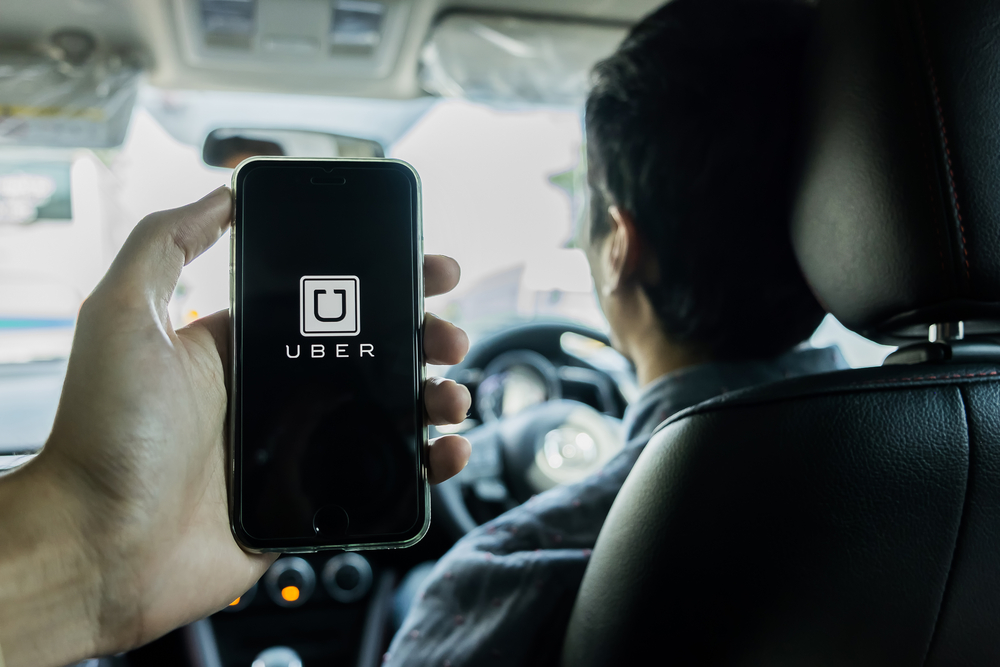 A man holding phone displaying Uber app sitting in the back of an Uber