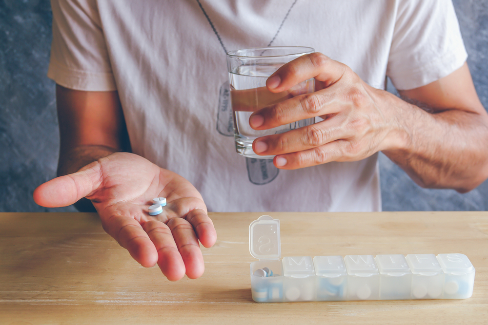 man holding 2 pills and a glass of water