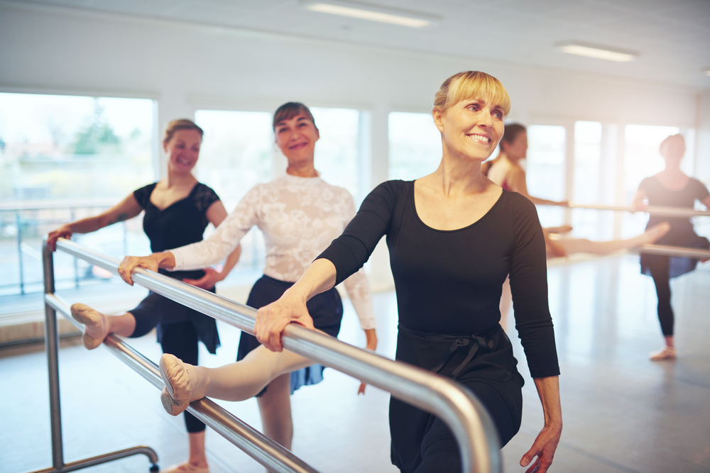 A group of adult women at the bar in a ballet studio.
