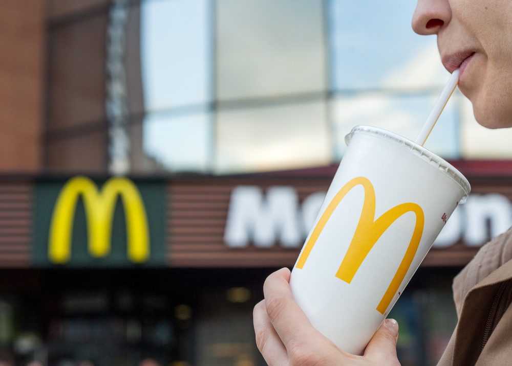 woman enjoying a sip from a McDonald's soft drink in front of a McDonald's location.