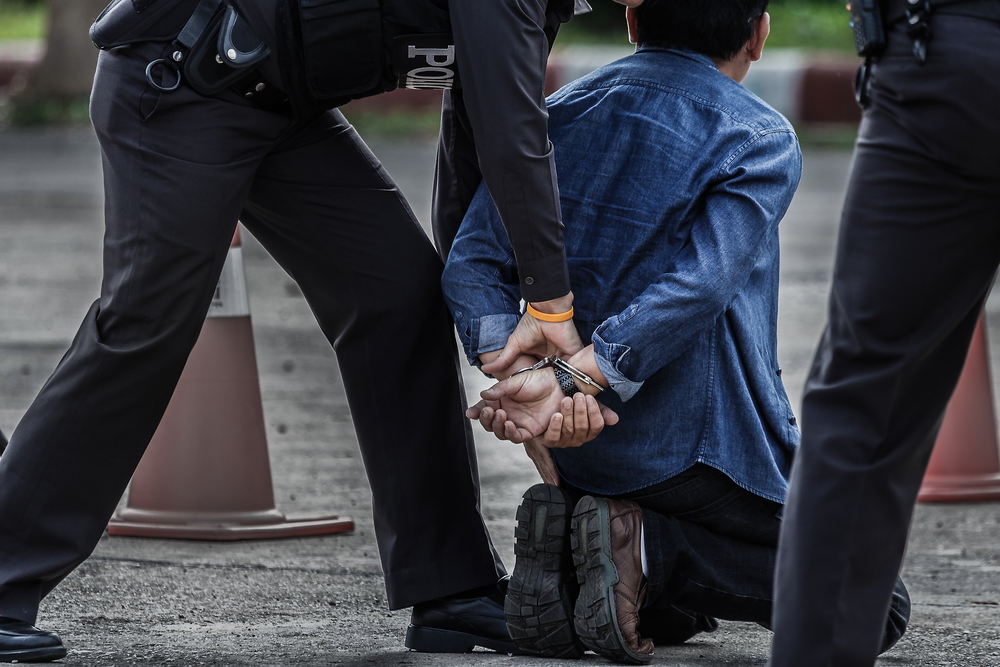 Man on his knees being handcuffed by police.