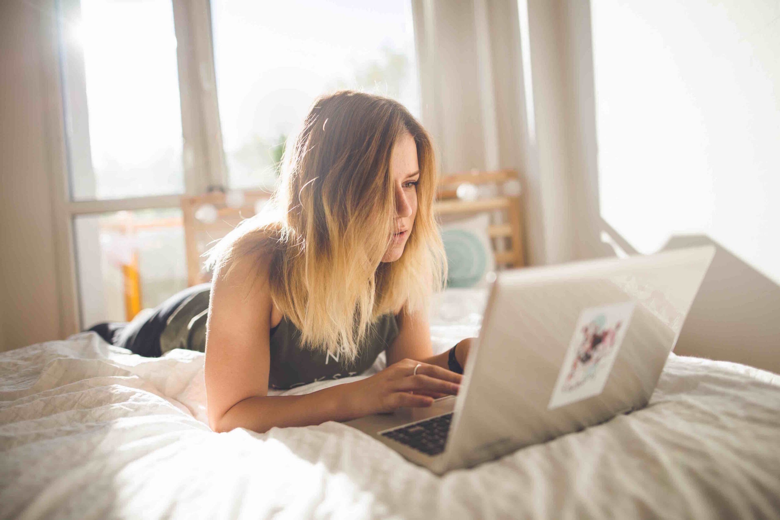 Woman lying on a bed, using a laptop.