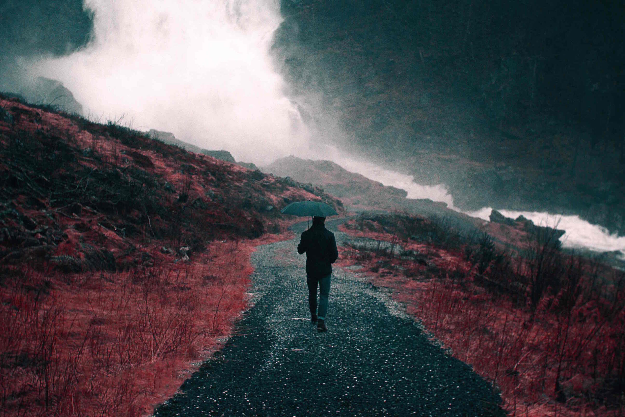 A man with umbrella walking down a road under cloudy and rainy sky