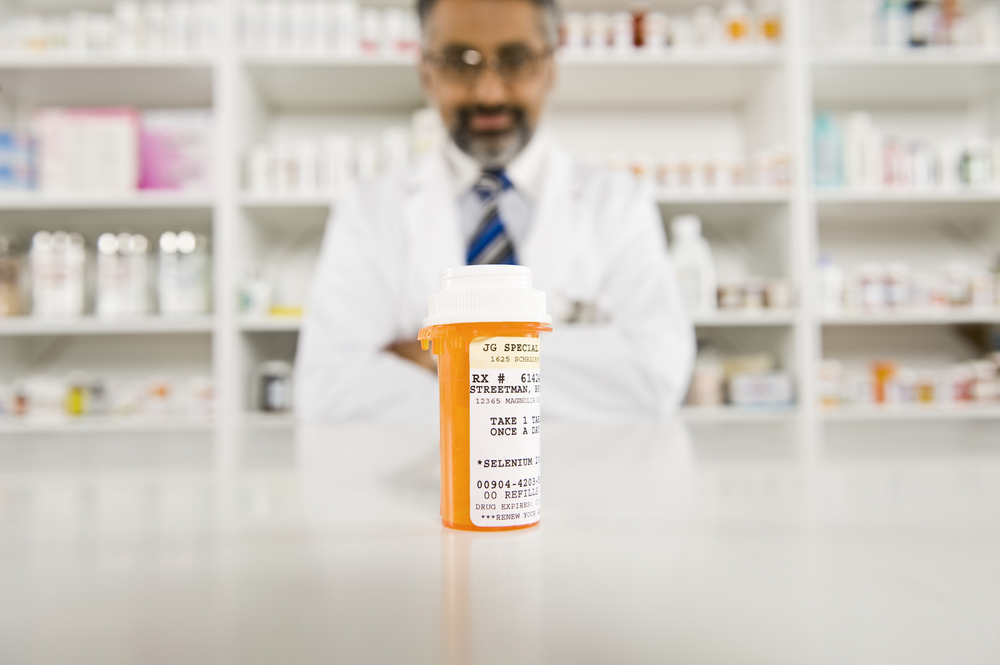 Bottle of pills on desk with a middle aged male pharmacist in the background