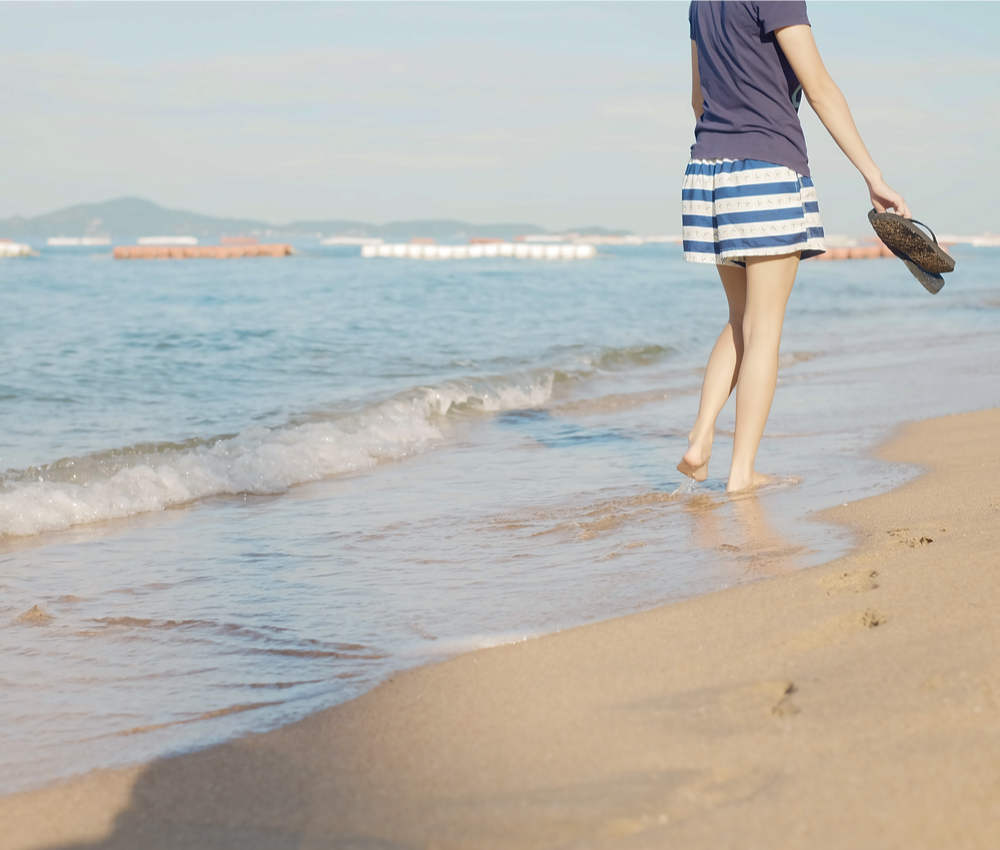 woman walking beach with sandals in hand