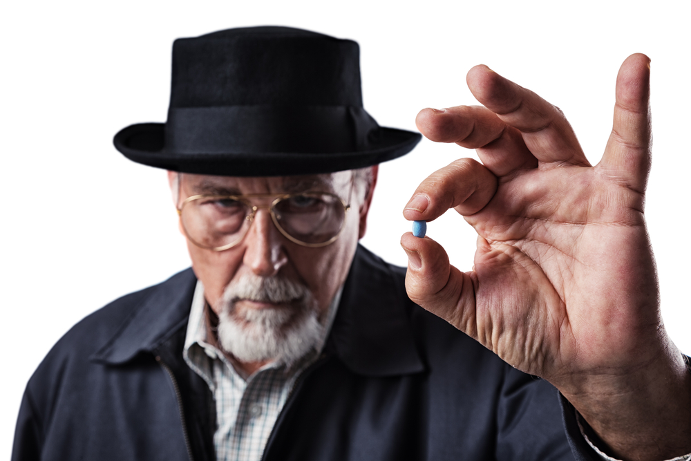 Old man holding a sample of male enhancement Viagra pill.