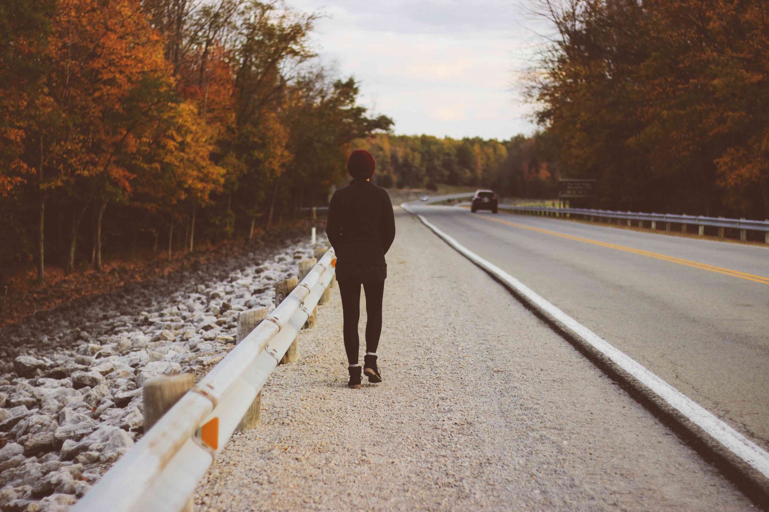 A person walking down a road, alone, facing away.