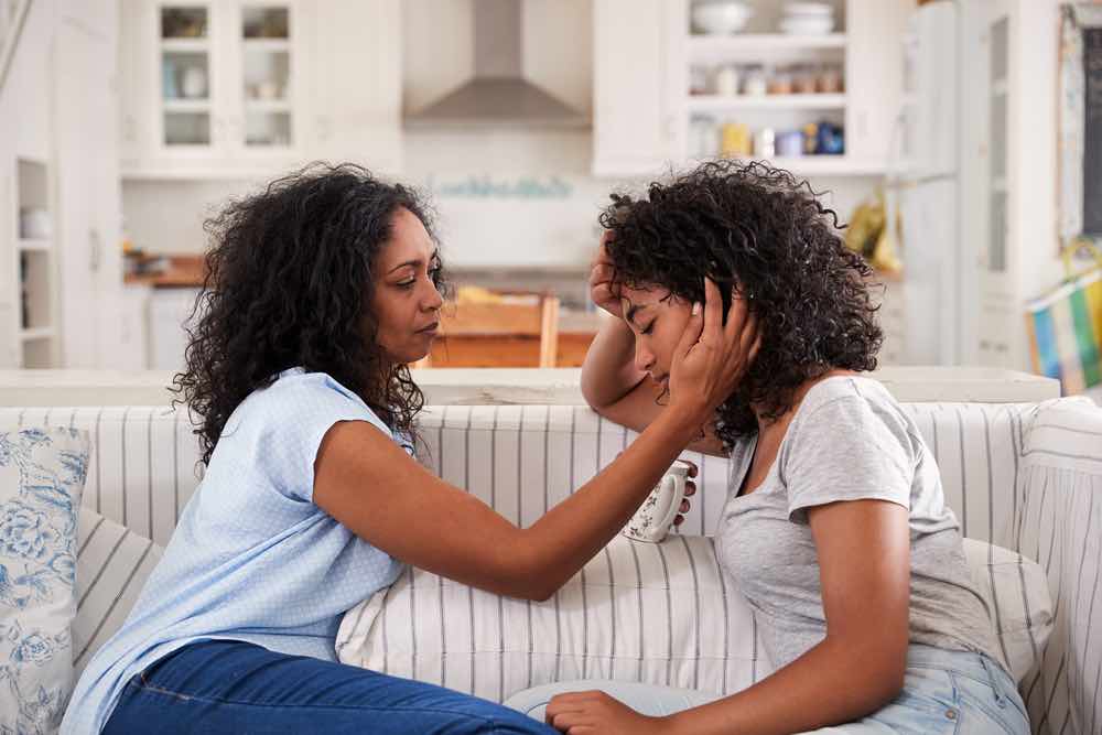 A mother comforts teenage daughter on couch.