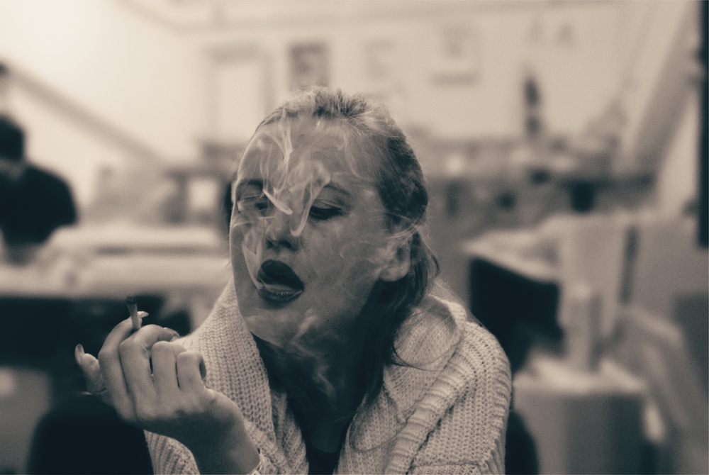 A black & white photo of a woman smoking a rolled cigarette in public