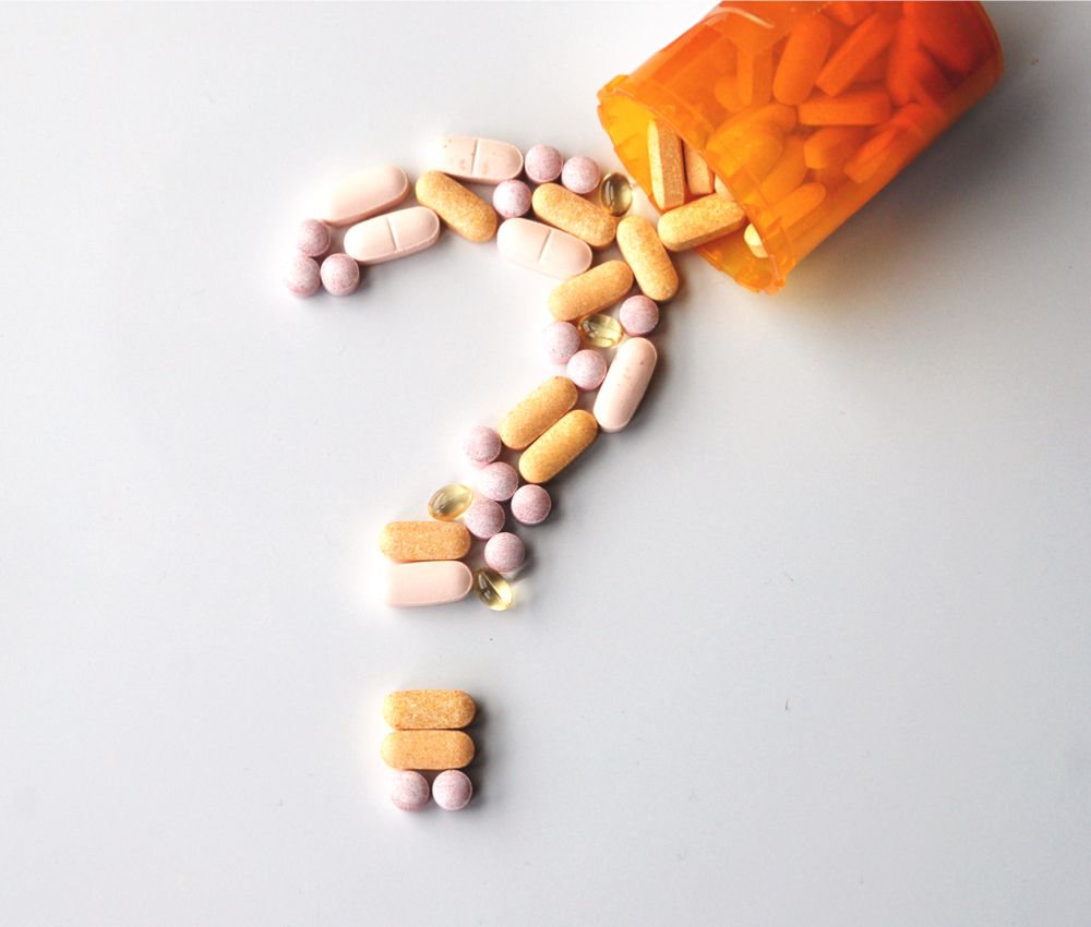 different drugs and health supplement pills in a question mark poured from a medicine bottle