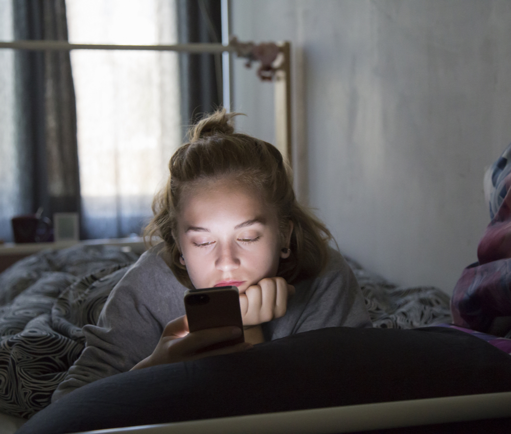 teenage girl checking her phone while in bed