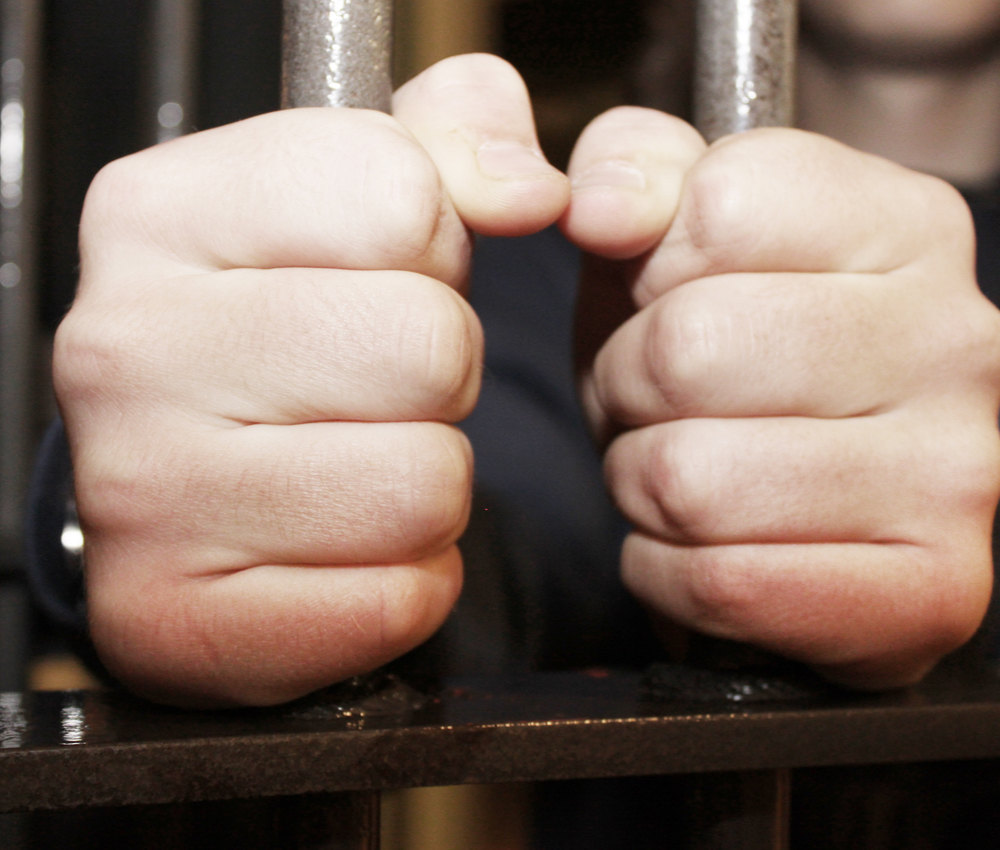 man's hands gripping prison bars