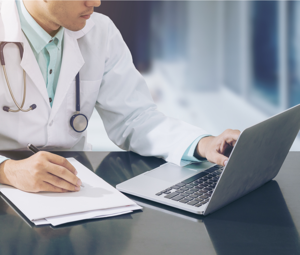 Doctor working with laptop computer and writing on paperwork.