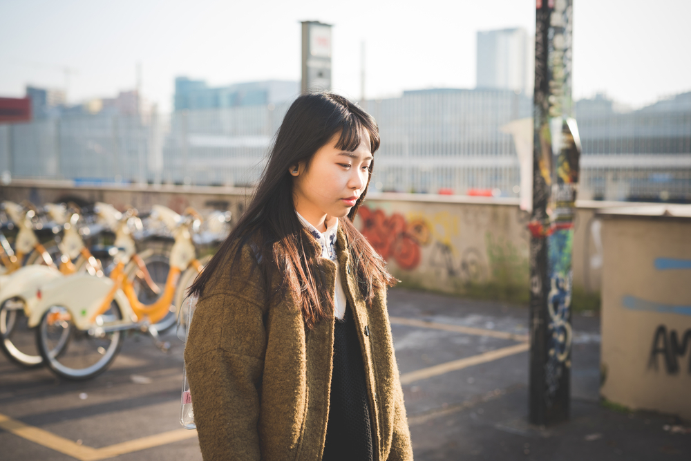 Woman in brown jacket walks past bikes at sunset