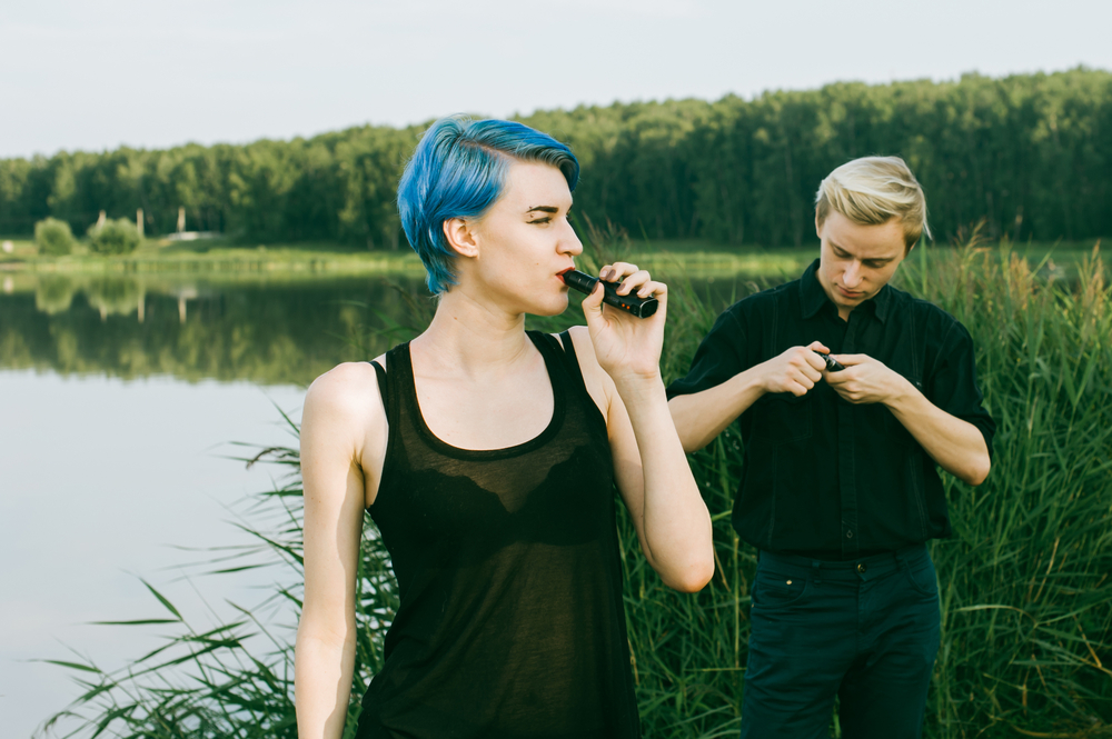 young couple with dyed hair smoking electronic cigarettes on the lake