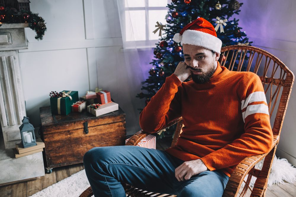 An unhappy man in a rocking chair in front of a Christmas tree.
