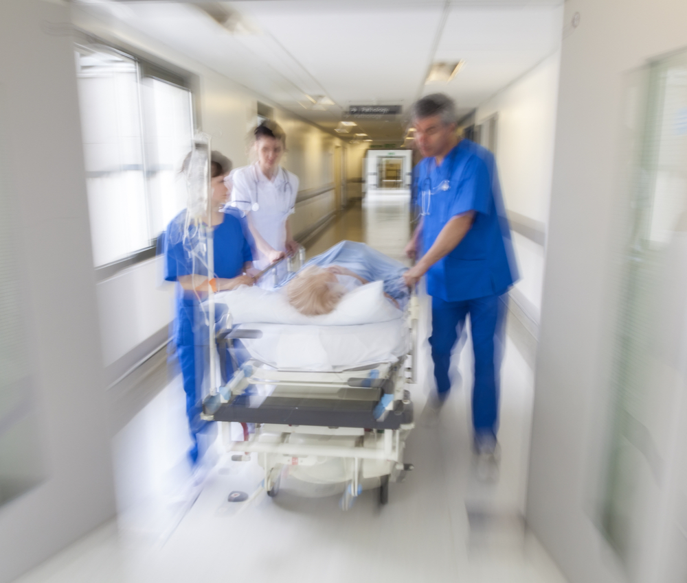 A motion blurred photograph of a patient on stretcher or gurney being pushed at speed through a hospital corridor by doctors & nurses to an emergency room