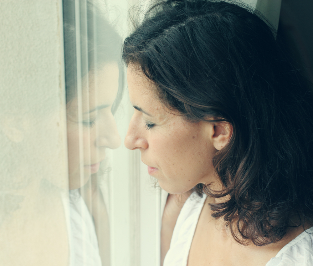sad woman standing in front of window