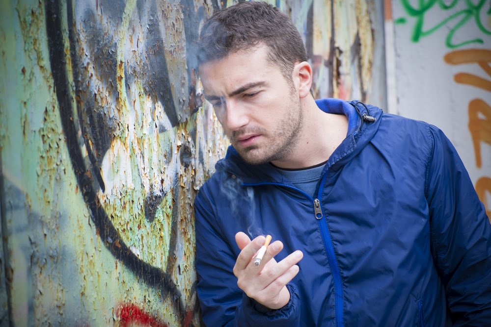 Man smoking cigarette leaning against wall.