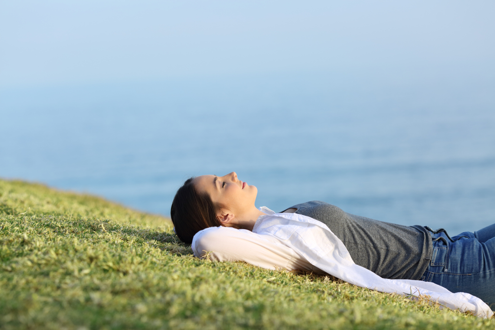 Side view portrait of a relaxed woman resting on the grass in the coast with the ocean in the background