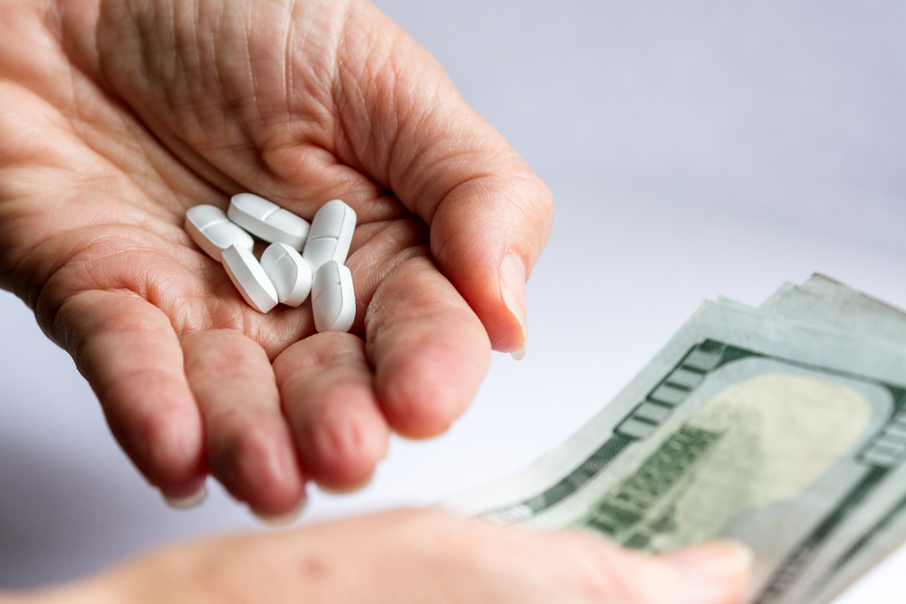 hands holding pain killer prescription opioids and another hand handing over three hundred US dollar bills
