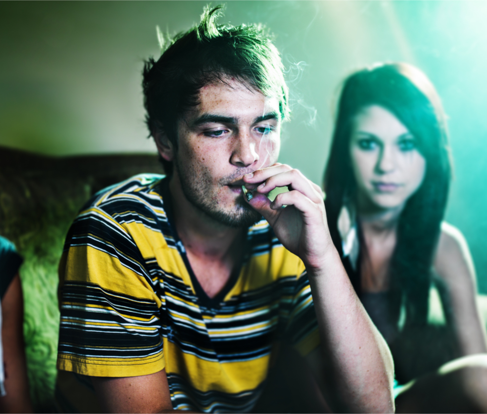 Guy smoking a marijuana joint while a girl watches him.