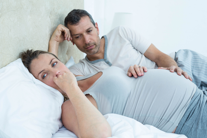 A man and a pregnant woman lying on a bed.