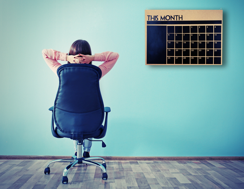 The back of a woman in an office chair looking at a calendar on the wall.