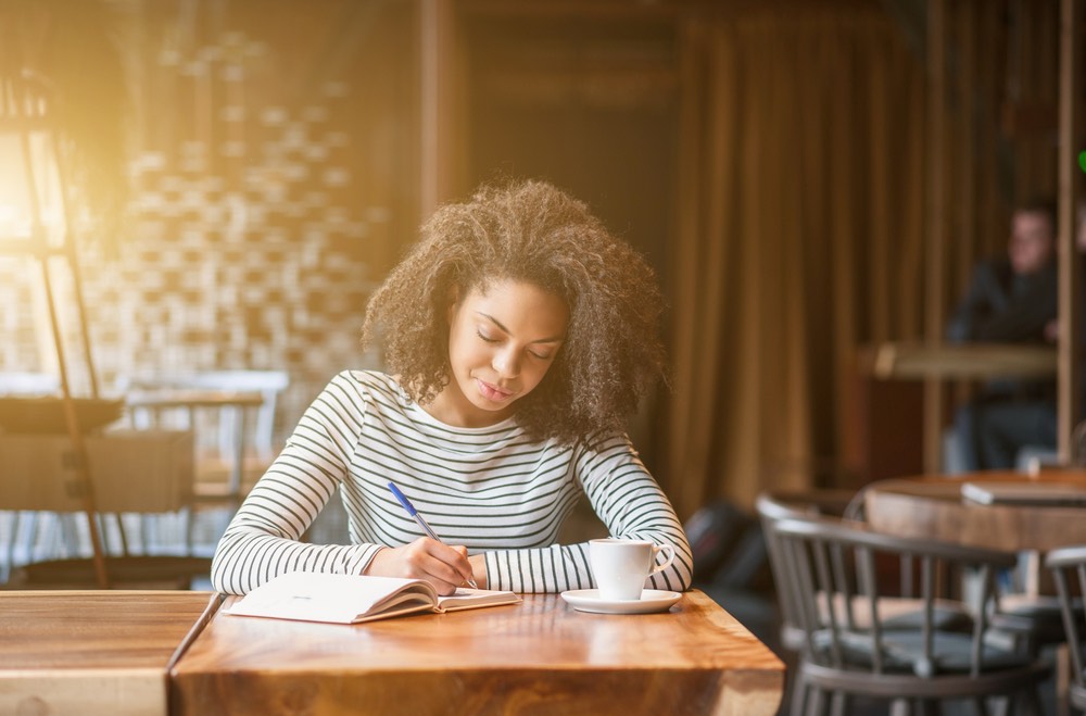 A woman writing in a journal, sitting in a cafe