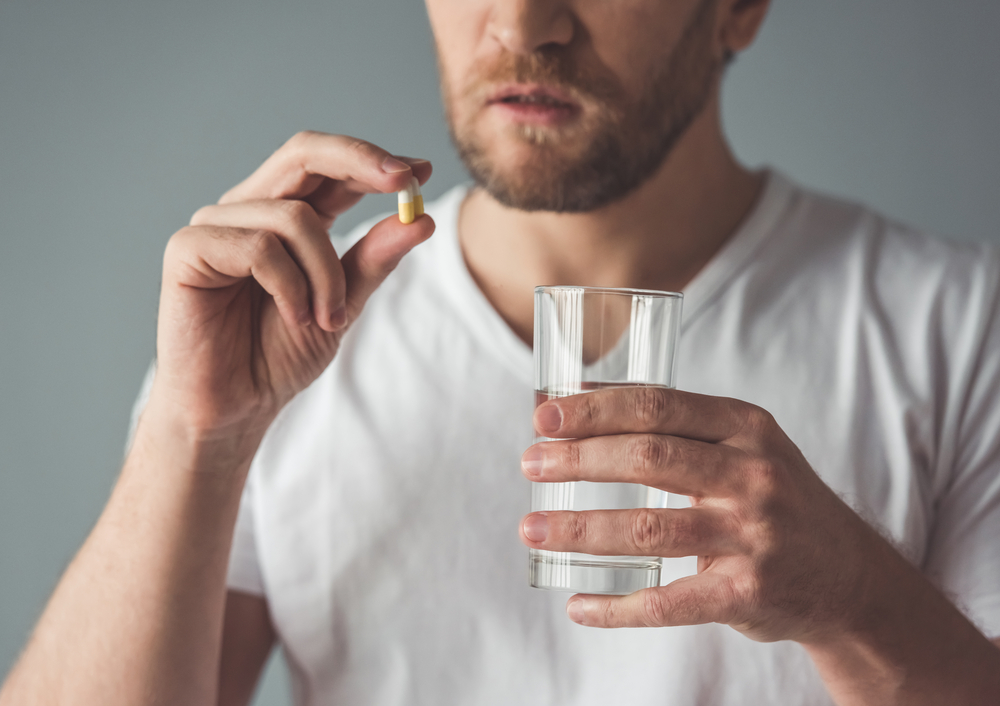 man holding a pill and a glass of water