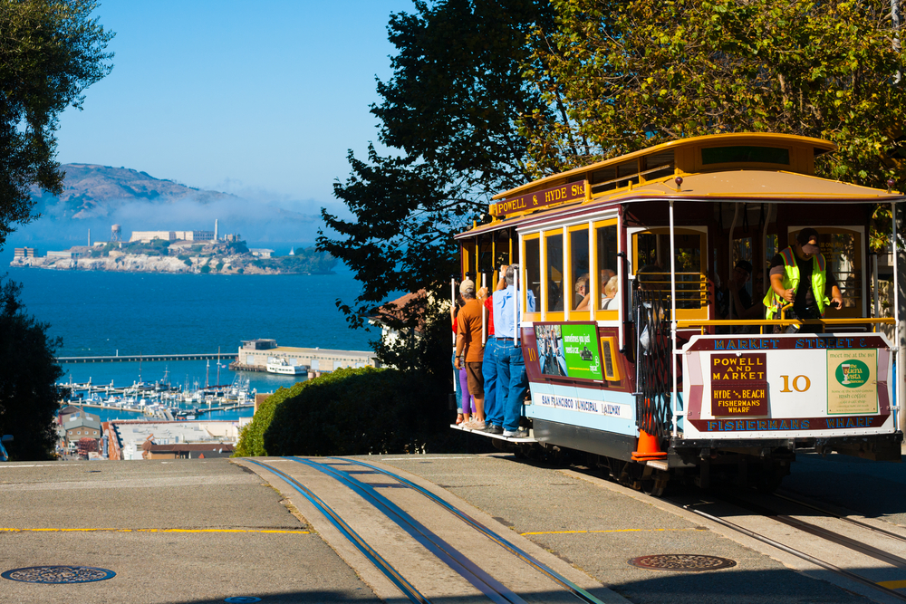 Powell Hyde cable car, an iconic tourist attraction, descending a steep hill peak overlooking Alcatraz prison island and the bay