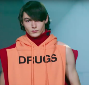 model wearing Raf Simon design that says "Drugs"