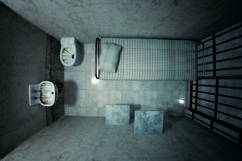 Top view of locked old prison cell for one person with bed, sink, toilet and chair. Dark atmosphere.