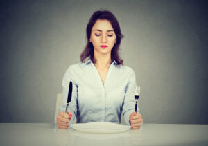 A serious woman sits with fork and knife and empty plate