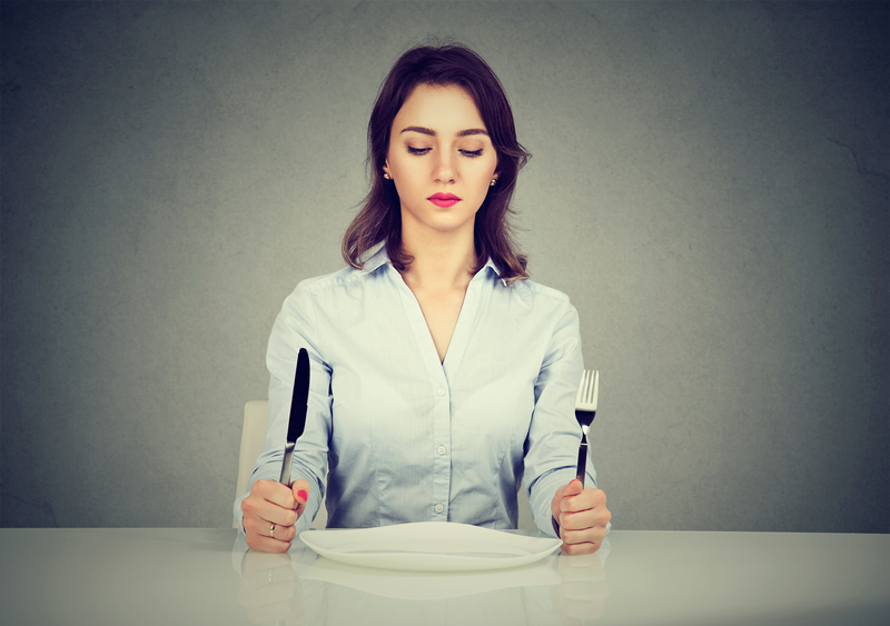 A serious woman sits with fork and knife and empty plate