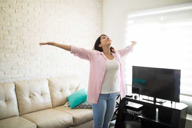 A woman in a clean apartment, arms held wide and head up.