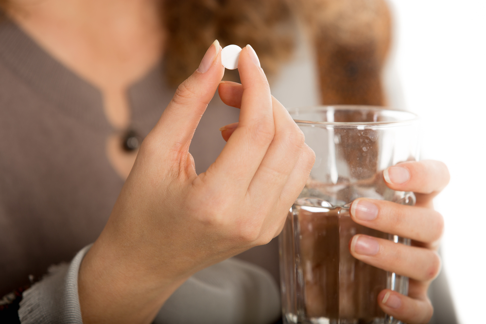 Female hands hold one pill and glass of water close-up