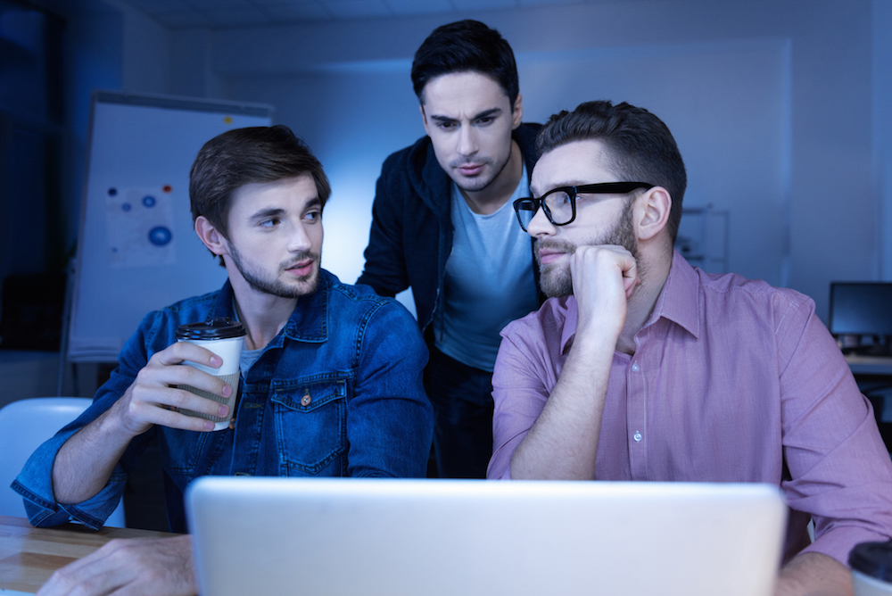 Group of college-aged men pondering near a laptop