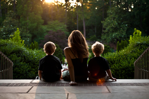 Back view of mother and two boys sitting and looking over wooded area.