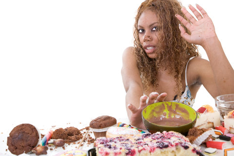 Woman with a lot of sweets on table, lifting hand to say enough.