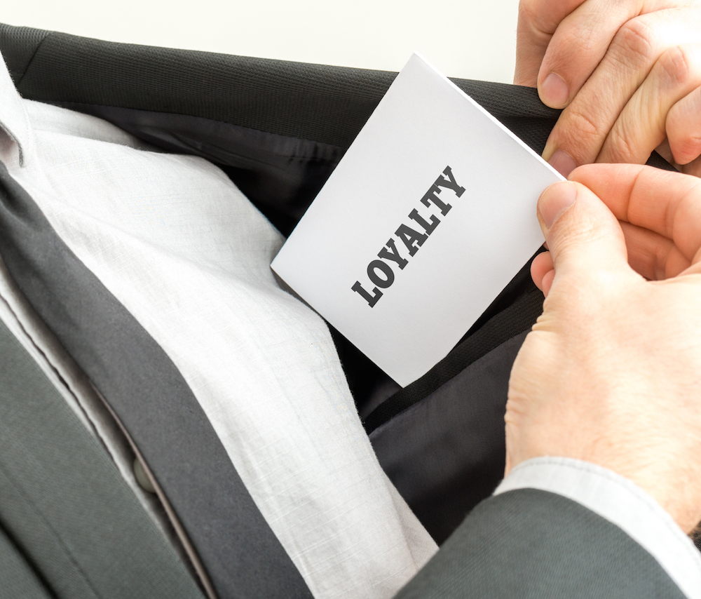 man withdrawing white card that says loyalty from his suit pocket
