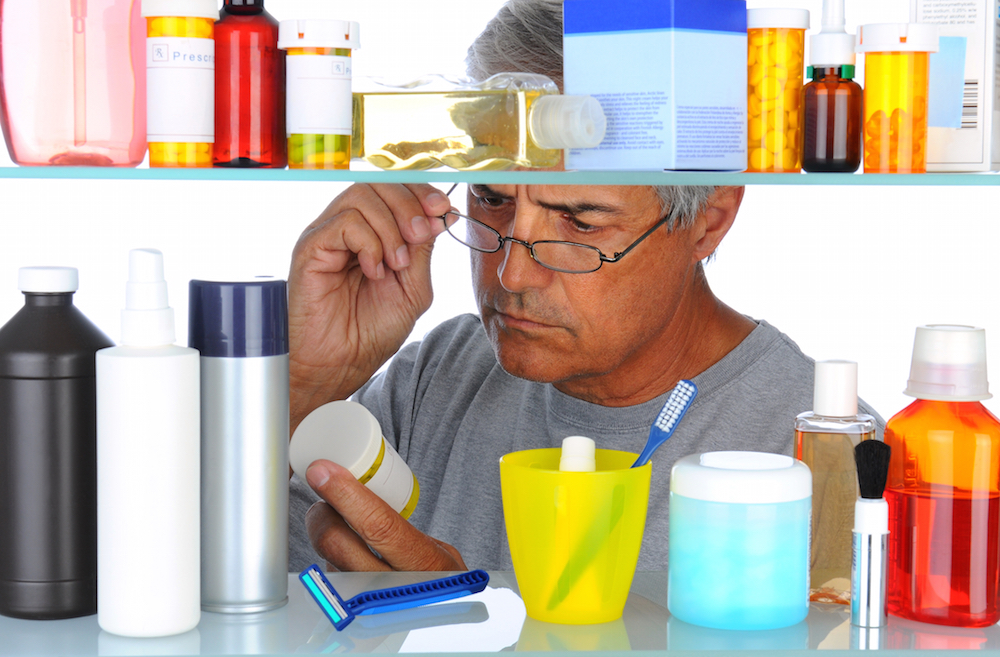Man examining prescription pill bottle in front of medicine cabinet