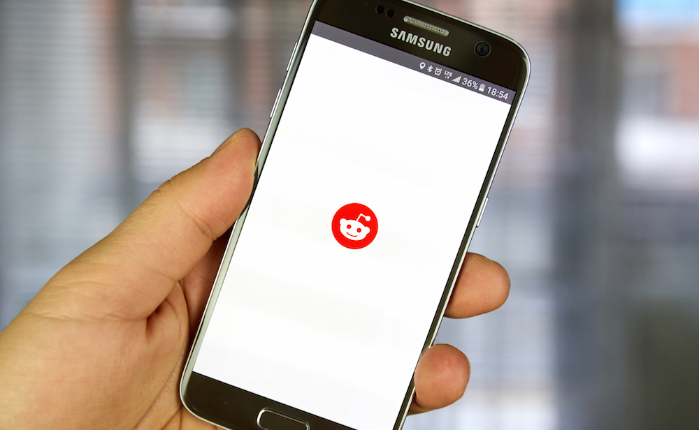 hand holding a phone and opening the Reddit app.