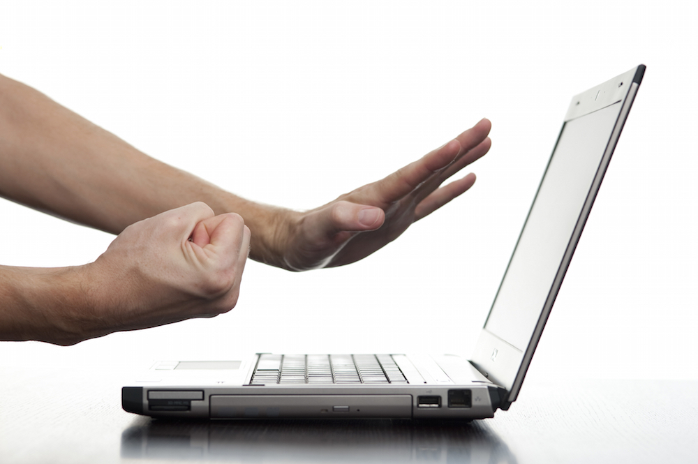 An angry man threatens his laptop computer with his fist,
