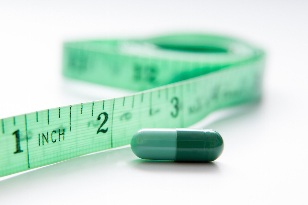a green measuring tape lying beside a pill capsule.
